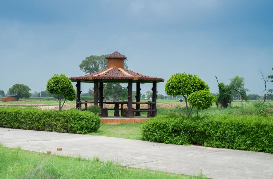 A gazebo beside a paved path and trimmed hedges at Shri Krishna Enclave