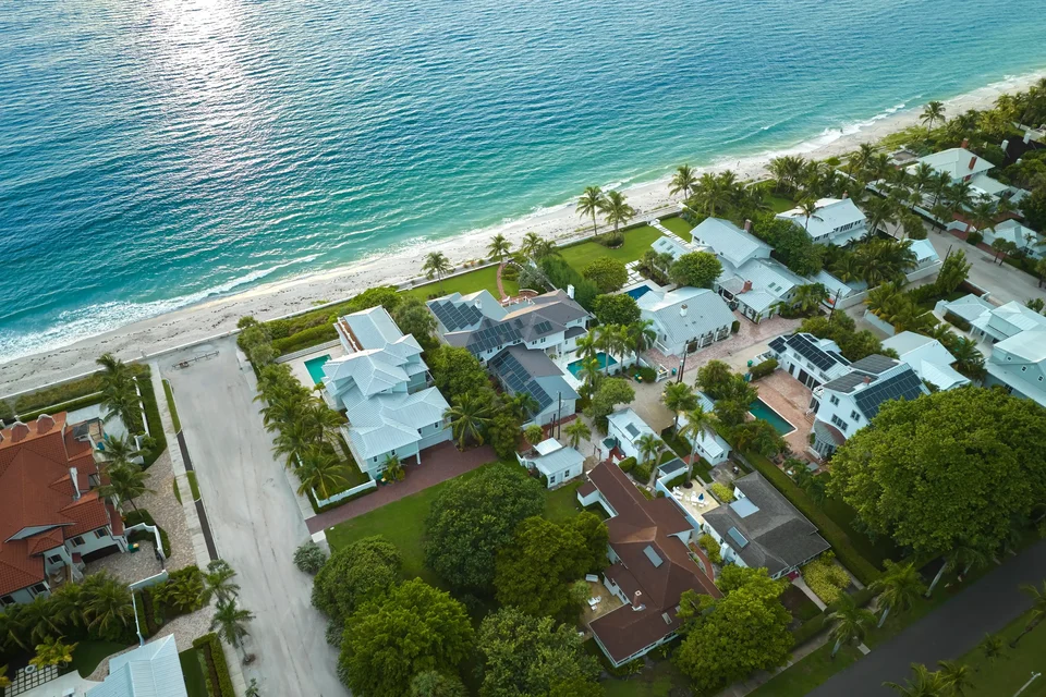 Aerial view of villas with private pools beside a beach and turquoise sea