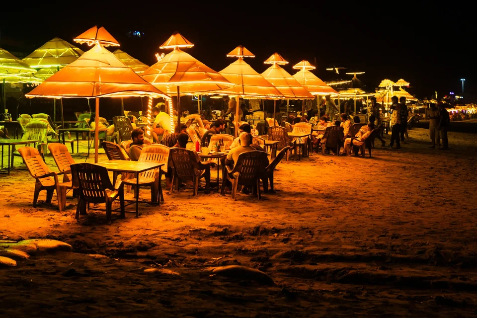 People dining under lit umbrellas at a beach shack at night