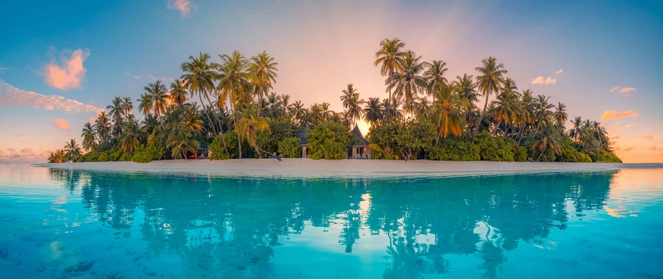 A palm-covered island in calm turquoise water at sunset