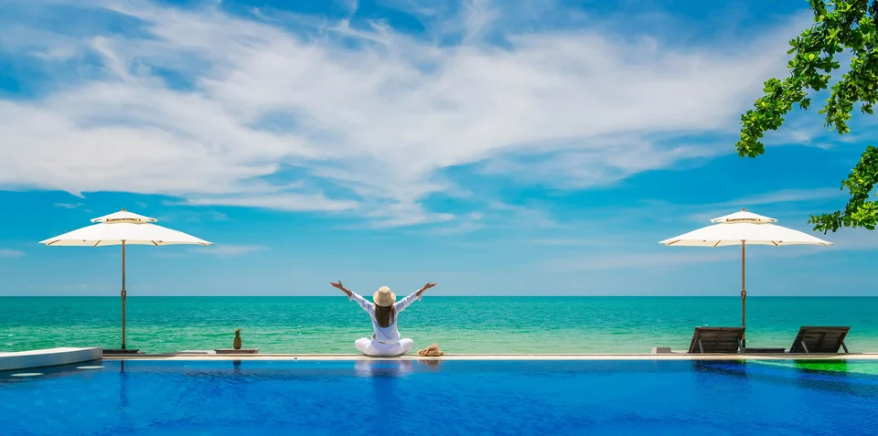 A woman with raised arms at the edge of an infinity pool facing the sea