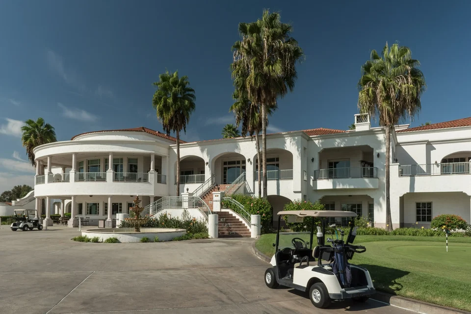 A white colonial-style clubhouse with palm trees and a golf cart in front