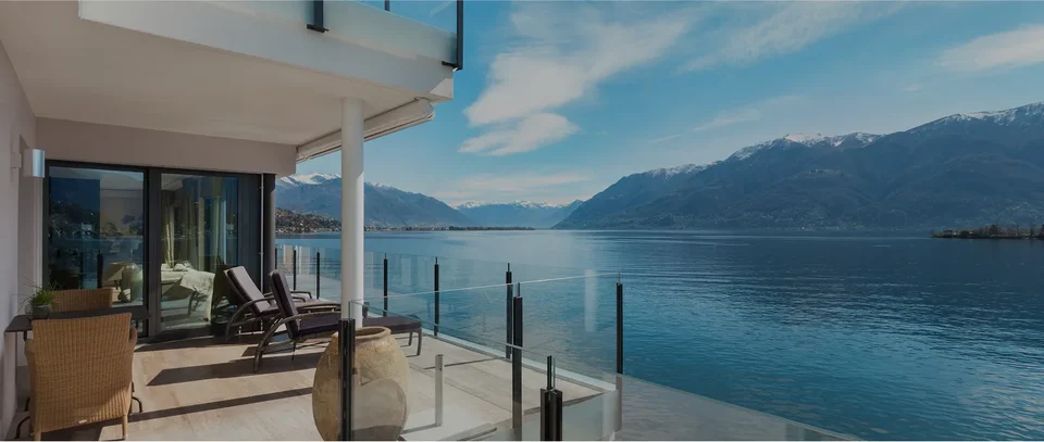 A villa balcony with a glass railing looking over a lake and mountains