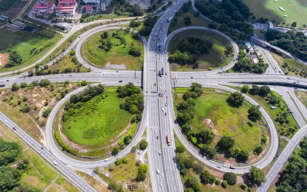 Aerial view of a cloverleaf highway interchange, with looping ramps circling patches of green and traffic moving along the main road.