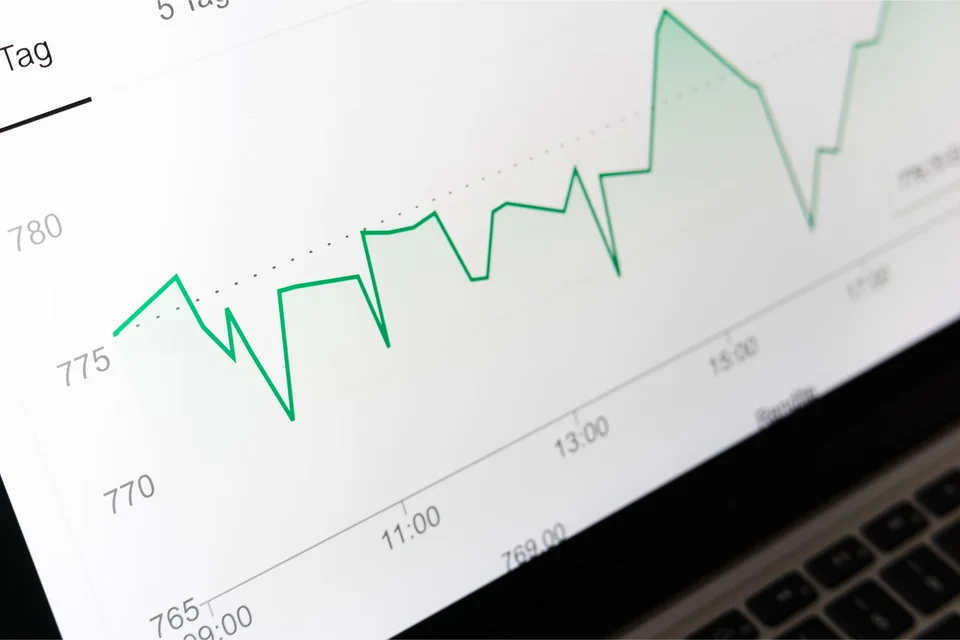 Close-up of a laptop screen showing a green line chart that fluctuates and climbs towards the right, with time markings along the bottom axis.