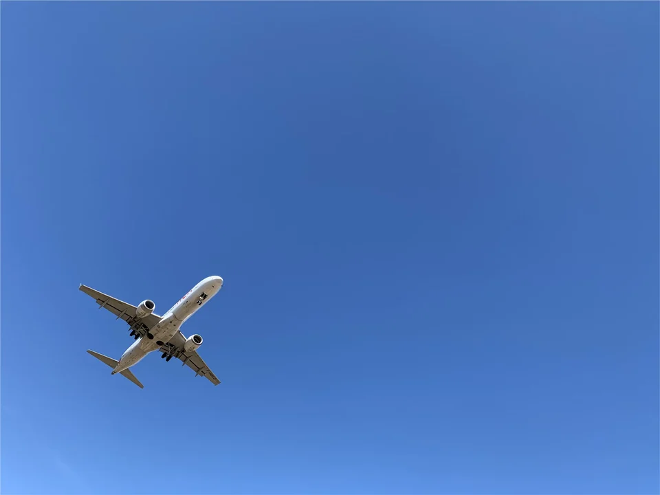 Passenger jet seen from below flying across a clear, deep blue sky.