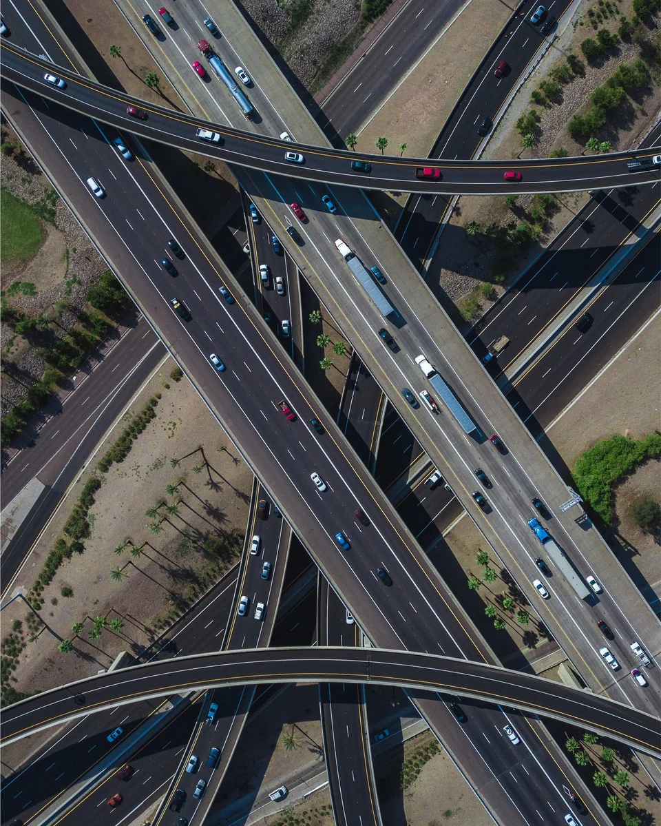 Aerial view of a multi-level highway interchange, with several elevated carriageways crossing and curving over one another and cars and trucks on every lane.