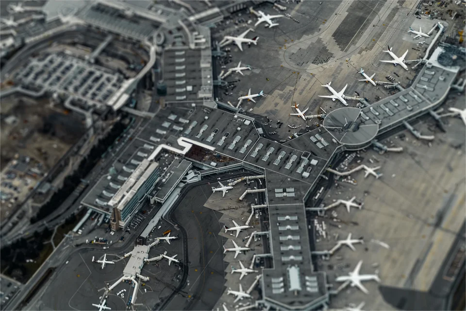 Tilt-shift aerial photograph of a busy airport terminal complex, with dozens of passenger jets parked at its gates and across the apron.