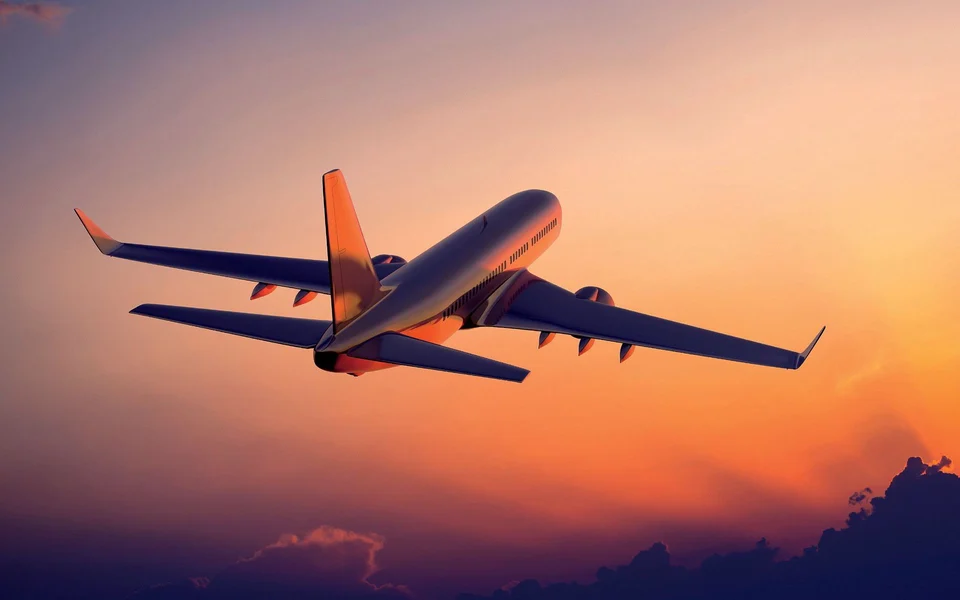 Passenger jet climbing into an orange sunset sky, seen from below and behind.